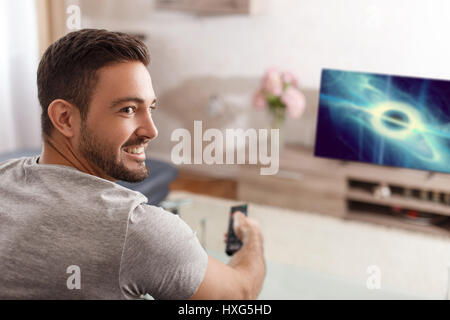 Excited man switch TV to sci-fi movie by remote control Stock Photo