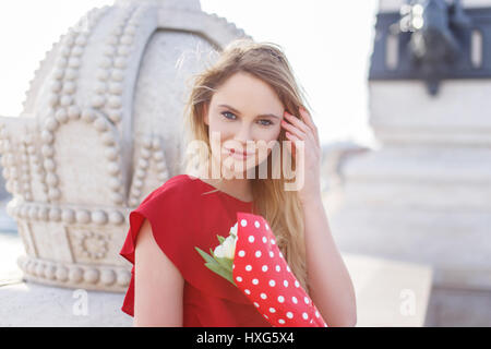 Young blonde caucasian woman in red dress with bouquet portrait Stock Photo