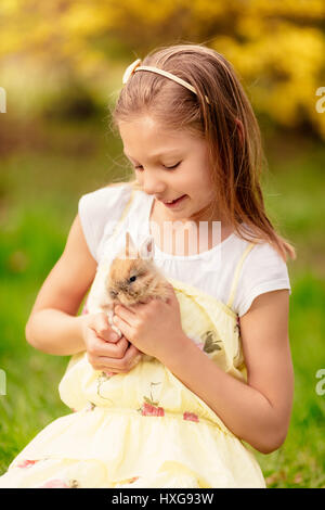 Beautiful smiling little girl holding cute bunny on nature in spring holidays. Stock Photo