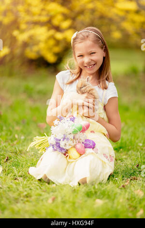 Beautiful smiling little girl holding cute bunny and bouquet white flowers and Easter eggs in spring holidays. Stock Photo