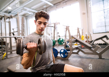 Young hispanic fitness man in gym sitting on bench, working out with weights Stock Photo