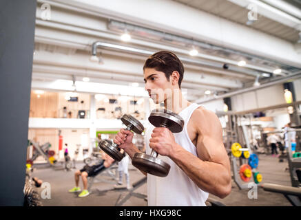 Handsome young hispanic fitness man in gym sitting on bench, working out with weights Stock Photo
