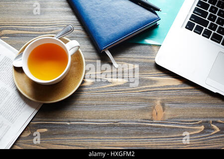 Closeup background shot of different business objects in cafe: laptop, documents and folders next to cup of tea left by working businessman on wooden  Stock Photo