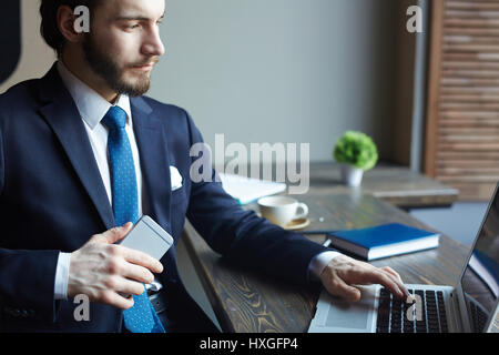 Portrait of handsome elegant businessman busy working with laptop and smartphone at wooden table in cafe Stock Photo