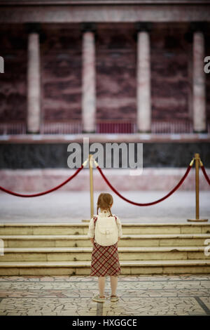 Little schoolgirl standing by red velvet rope in museum Stock Photo
