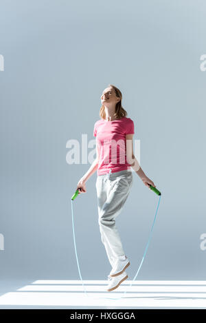 side view of sporty woman exercising with skipping rope on grey Stock Photo