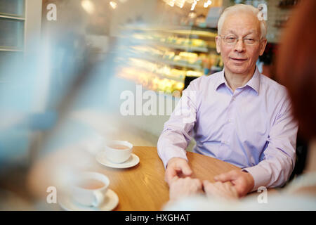 Senior grey-haired man holding his wife by hands while relaxing in cafe Stock Photo