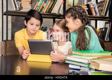 Three smiling schoolchildren using digital tablet in library Stock Photo