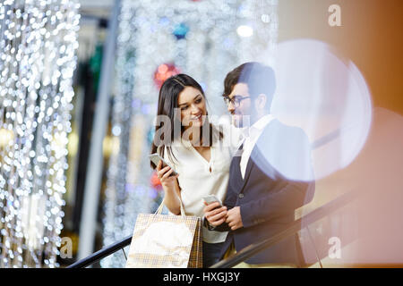 Woman with smartphone carrying paperbags and talking to businessman on escalator in the mall Stock Photo