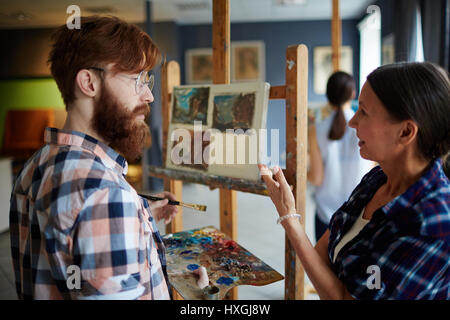 Experienced teacher consulting her student and pointing at his painting Stock Photo