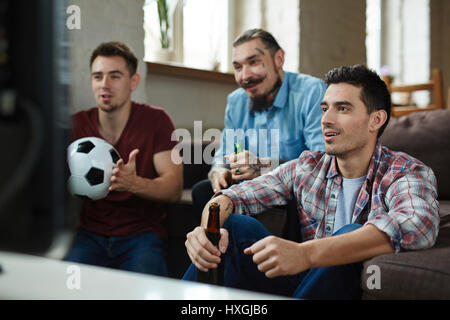 Group of friends watching football match on TV while sitting on couch and drinking beer Stock Photo