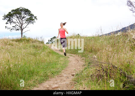 Full length portrait of athletic woman running on dirt path outdoors in park Stock Photo