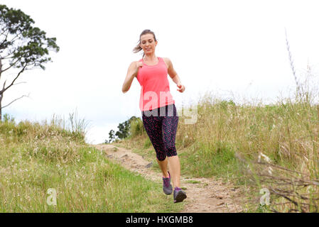 Full length portrait of sporty woman running on dirt path outdoors in park Stock Photo