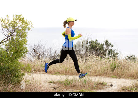 Full length side portrait of sporty woman running on dirt path Stock Photo