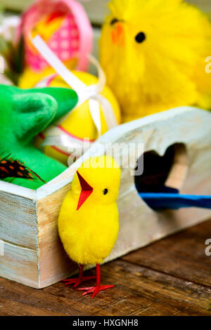 closeup of some some toy chicks and some different decorated easter eggs in a rustic wooden tray, on a wooden surface Stock Photo