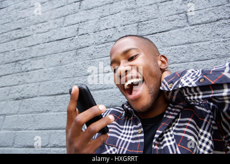 Close up portrait of young african man laughing after reading a funny text message on his mobile phone Stock Photo