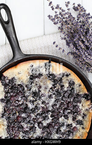 Above image of a blueberry lavender cobbler baked in a cast iron skillet over a white wood table top. Image shot from overhead. Perfect dessert for sp Stock Photo