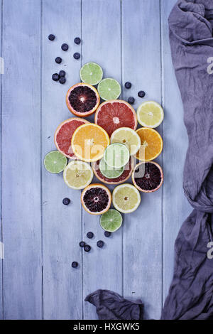 Variety of citrus fruits (orange, blood oranges, lemons, grapefruits, and limes) with blueberries with grey fabric over a blue rustic wood table top.  Stock Photo