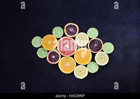 Variety of citrus fruits (orange, blood oranges, lemons, grapefruits, and limes) over a black rustic background. Image shot from overhead. Stock Photo