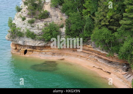 Breathtaking cliff view with crystal clear blue water and green trees.   Above the water is a cave in Pictured Rocks National Park In Upper Michigan. Stock Photo