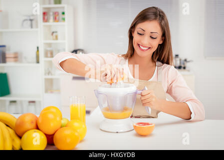 Beautiful young woman in the kitchen squeezing orange juice with an electric juicer. Stock Photo