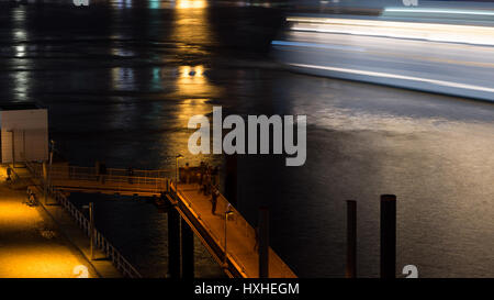 Abstract long exposure of people watching a cruise ship leaving the harbor of Hamburg, Germany at night. Stock Photo