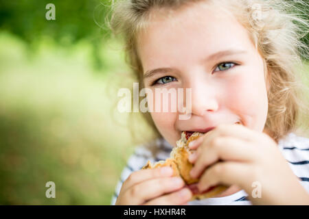 Girl eating snack bun at the park in summer out of hunger Stock Photo