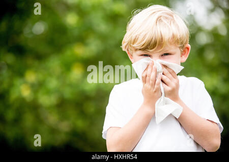 Child with allergy cleaning his nose with tissue in the nature Stock Photo