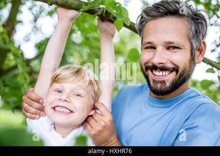 Father supports son with gymnastics while boy climbs tree Stock Photo