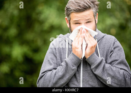 Man with allergy or ill with hay fever sneezing and cleaning nose