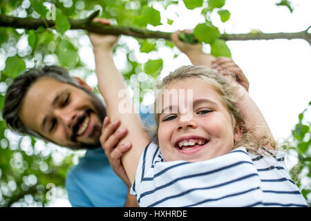 Girl plays and has fun with father climbing tree in the nature