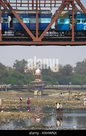 A train crossing the Yamuna River in Agra, with discarded garbage being scavenged below Stock Photo