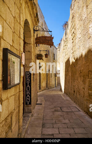 MDINA, MALTA - JULY 29, 2015: The narrow medieval stone paved street with the restaurant “Medina” in the Mdina, the old capital of Malta Stock Photo