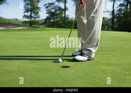 Golfer taps in with putter on a green with trees near a lake Stock Photo