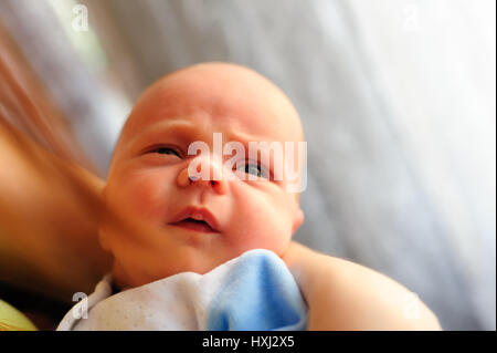 Cute baby girl makes a funny upset face on mothers hand Stock Photo