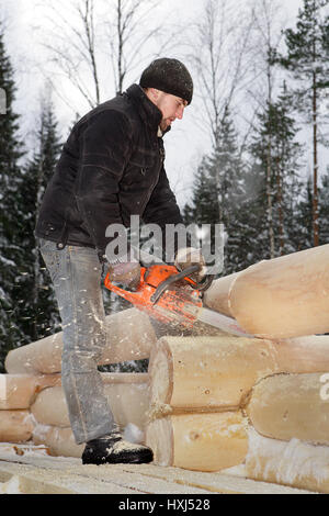 Leningrad Region, Russia - February 2, 2010: Construction of log house, a young worker sawed timber, using a chainsaw. Stock Photo