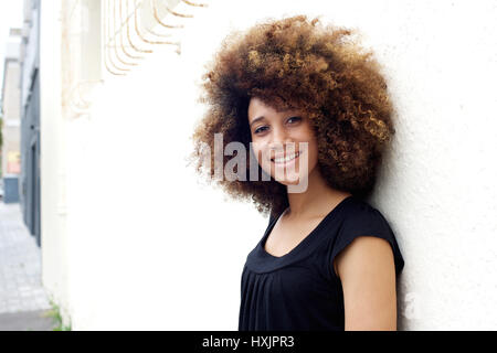 Portrait of happy young african american girl leaning on a white wall Stock Photo