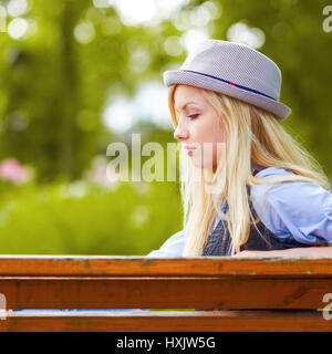 Thoughtful hipster girl sitting on bench in the park Stock Photo