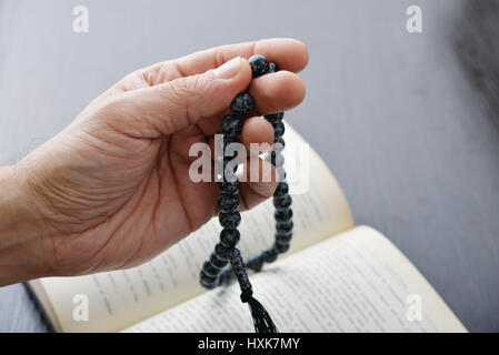 Male hand holding rosary beads closeup and koran on background. Stock Photo