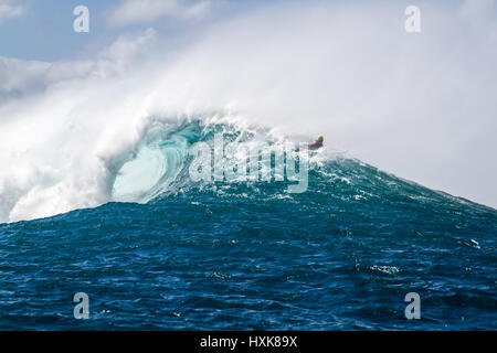 A Surfer paddles over a giant Ocean wave on the north shore of Oahu Hawaii at an outer reef surf break Stock Photo