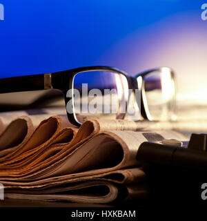 Glasses on stack of newspapers against blue screen Stock Photo