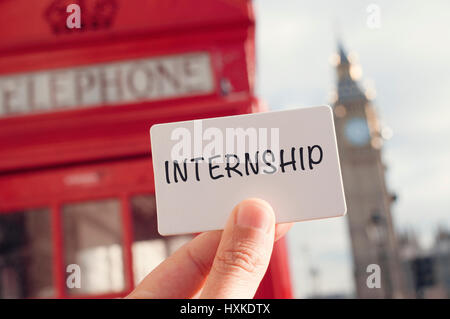 the hand of a young man showing a signboard with the word internship with a red telephone booth and the Big Ben in the background, in London, United K Stock Photo