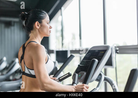 Fit Woman Using Elliptical Trainer in Modern Gym Stock Photo