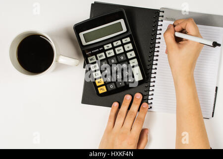 Woman's hand writing in a book with a cup of coffee and calculator Stock Photo
