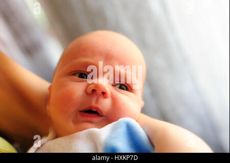 Cute baby girl makes a funny upset face on mothers hand Stock Photo