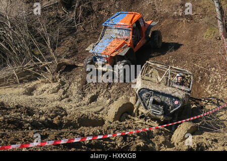 All-terrain vehicle will bi pushed uphill from a mud with steel wire by hydraulics of excavator, a four-wheel drive is driving towards muddy trench Stock Photo