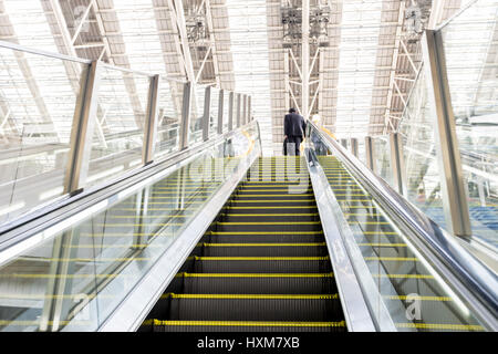 Businessman going up an escalator with luggage Stock Photo