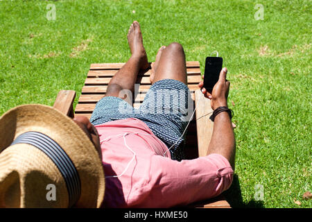Portrait of man lying on lounge chair holding a mobile phone on a summer day Stock Photo