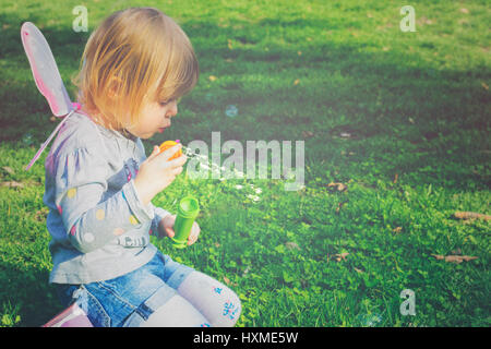 Toddler girl with butterfly wings having fun in park, blowing soap bubbles Stock Photo