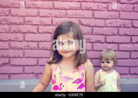 Portraits of two little girls in front pink brick wall Stock Photo